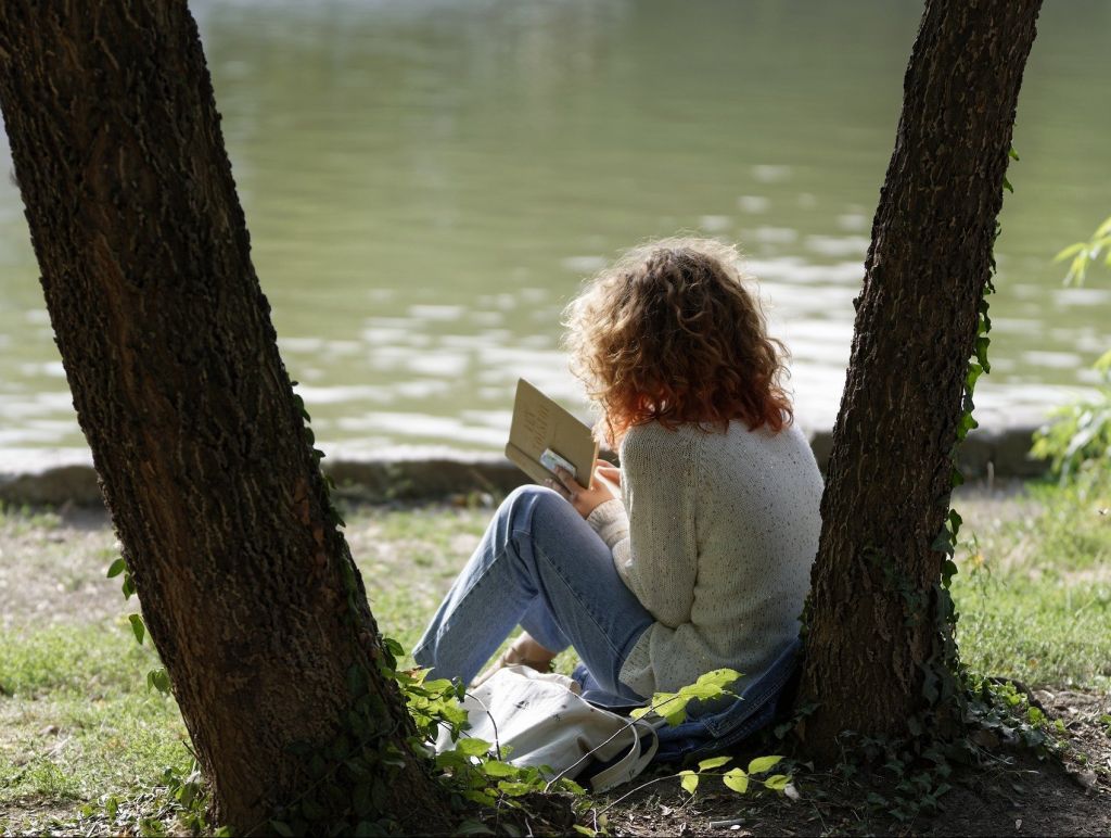 Mädchen liest Buch zwischen Bäumen